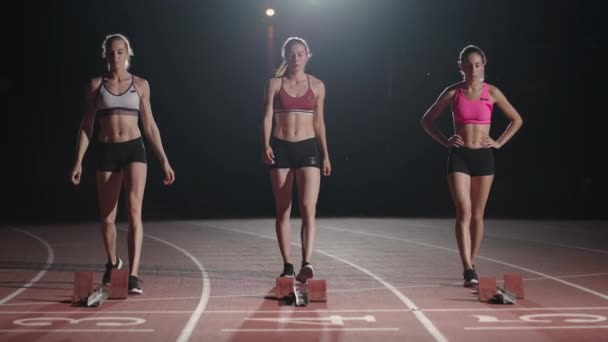 Drei Läuferinnen bereiten sich darauf vor, im Stadion in Zeitlupe im dunklen Licht zu laufen - Filmmaterial, Video