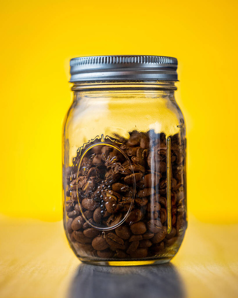 A closeup shot of a glass jar with coffee beans on a yellow background - Foto, immagini