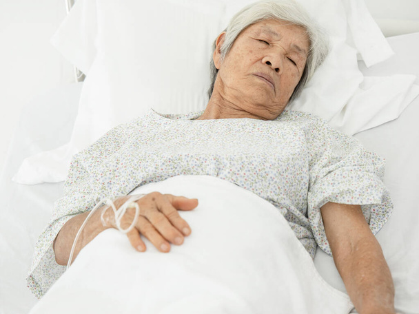  Ältere Patientin liegt mit intravenösem Flüssigkeitströpfchen in der Hand auf dem Bett, Gesundheitsversorgung und medizinisches Konzept - Foto, Bild