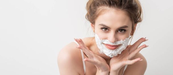 Retrato de una hermosa joven mujer caucásica sonriente con espuma de afeitar en la cara posa sobre fondo blanco - Foto, Imagen