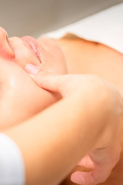 Beautician making lymphatic drainage face massage or facelifting massage at the beauty salon - Valokuva, kuva