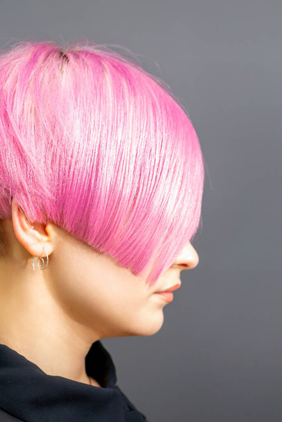 Profile portrait of a young caucasian woman with pink bob haircut isolated on a gray background - Photo, Image