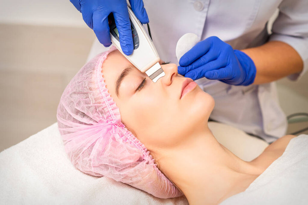 Closeup of beautiful young woman receiving ultrasound facial exfoliation and cavitation facial peeling with ultrasonic equipment in cosmetology office - Photo, Image