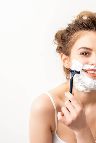 Portrait of beautiful young smiling caucasian woman shaves face with razor on white background - Foto, Imagen