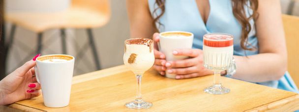 Egy fiatal nő kezei, kezében egy csésze kávéval, különböző koktélokkal az asztalon a kávézóban. - Fotó, kép