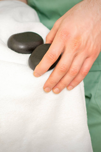 Primo piano delle salviette per le mani del massaggiatore pietre da massaggio nere con un asciugamano bianco - Foto, immagini