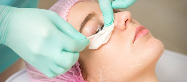 Young woman receiving eyelash removal procedure and removes mascara with a cotton swab and stick in a beauty salon - Fotografie, Obrázek