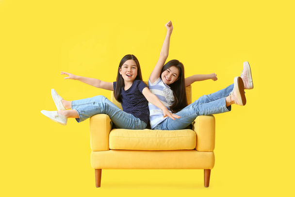 gelukkig zusjes zitten op fauteuil tegen kleur achtergrond - Foto, afbeelding