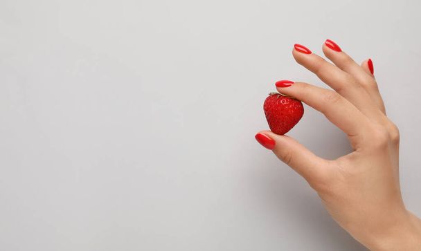 Weibliche Hand mit schöner Maniküre hält Erdbeere auf hellem Hintergrund - Foto, Bild