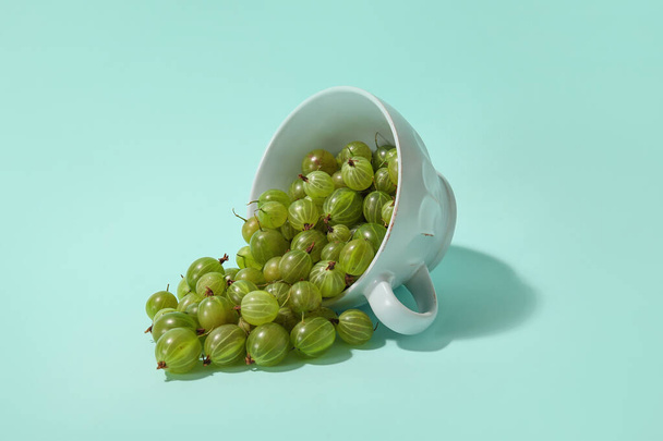 Coppa con uva spina matura fresca su sfondo di colore - Foto, immagini