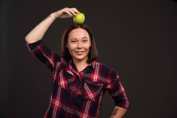 Female model in fall winter collection outfits holding a green apple on the head . High quality photo - Photo, Image
