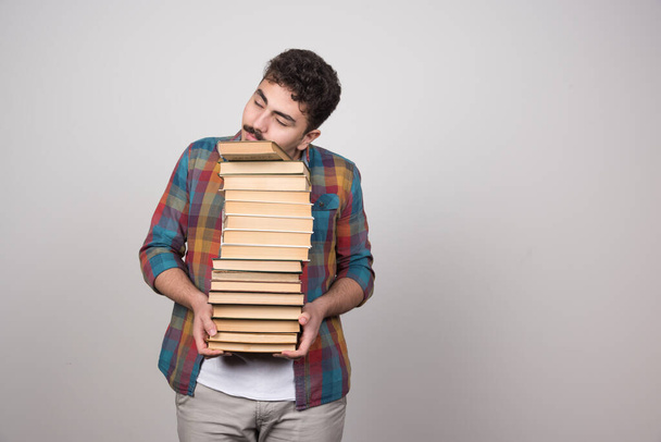 Mladý muž drží hodně knih na šedé zdi. Kvalitní fotografie - Fotografie, Obrázek