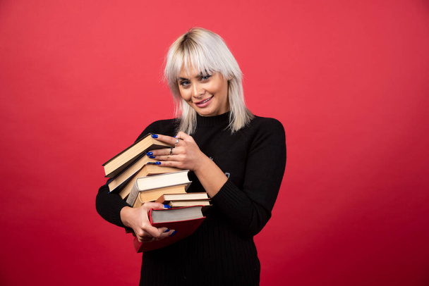 Young woman model holding a lot of books on a red background. High quality photo - Foto, Imagem