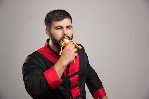 Νεαρός τρώει μπανάνα σε γκρι φόντο. Υψηλής ποιότητας φωτογραφία - Φωτογραφία, εικόνα
