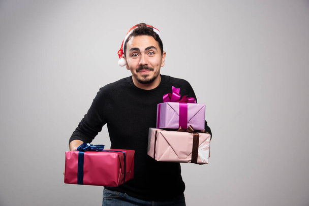 A young man holding gift boxes over a gray wall. High quality photo - Foto, Imagen