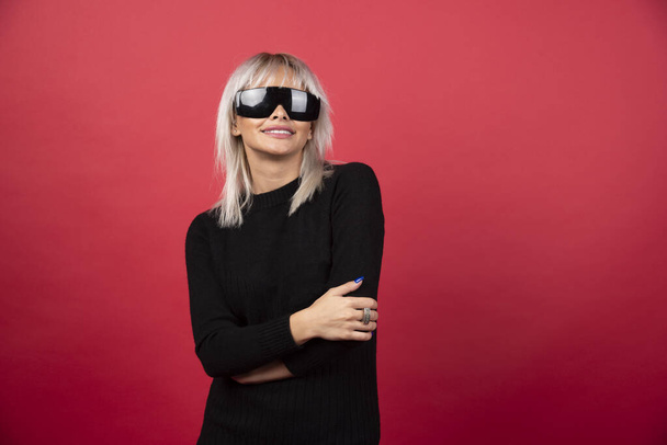Portrait of woman standing and posing with a black glasses on a red background.High quality photo - Foto, imagen