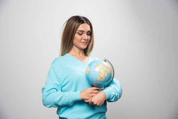 Fille blonde en sweat-shirt bleu tenant un globe, devinant l'emplacement et s'amusant. Photo de haute qualité - Photo, image