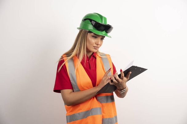 Worker woman industry in vest looking on clipboard - Фото, изображение