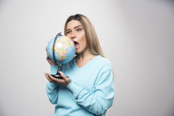 Blonde girl in blue sweatshirt holds a globe and bites it. High quality photo - Foto, immagini