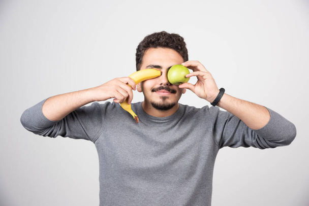 Młody człowiek trzymający banana i zielone jabłko. Wysokiej jakości zdjęcie - Zdjęcie, obraz