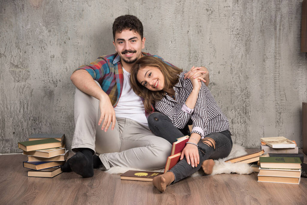 Φωτογραφία του νεαρού ζευγαριού που κάθεται στο πάτωμα με βιβλία. Υψηλής ποιότητας φωτογραφία - Φωτογραφία, εικόνα