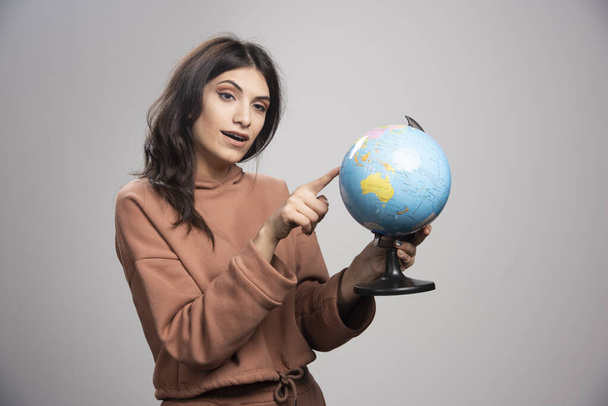 Brunette woman pointing at small place on globe. High quality photo - Foto, afbeelding
