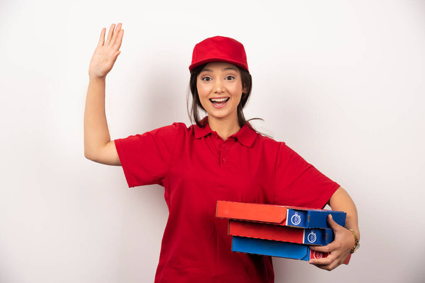 Happy female pizza delivery worker standing in white background with three cardboards of pizza. High quality photo - Photo, Image