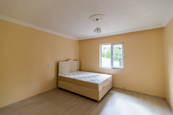 A bed and a chandelier in a yellow empty room - Фото, изображение