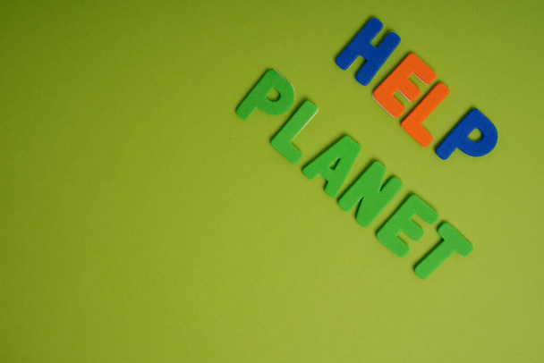 A closeup of a colorful writing on a green background that reads "help planet"- climate change concept - Φωτογραφία, εικόνα