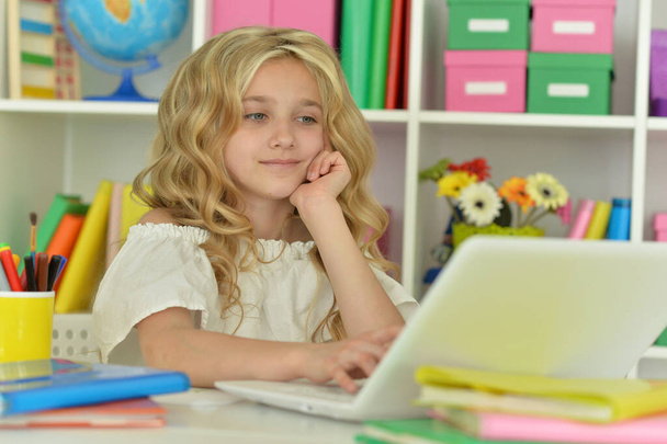 Cute girl ding home work with laptop at desk - Foto, Imagem