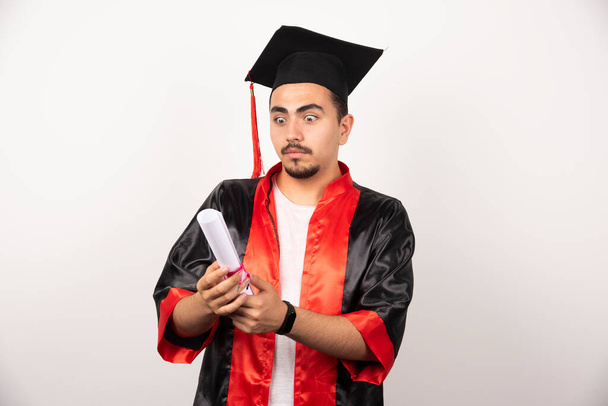 Młody absolwent wyglądający na zaskoczonego dyplomem na białym tle. Wysokiej jakości zdjęcie - Zdjęcie, obraz