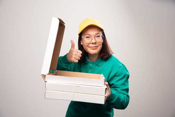 Deliverywoman showing a thumb up and holding cardboards of pizza on a white background. High quality photo - Photo, Image
