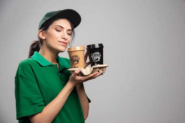 Delivery woman smells cups of coffee. High quality photo - Photo, Image