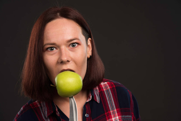Female model in fall winter collection outfits biting a green apple on the knife. High quality photo - Photo, Image