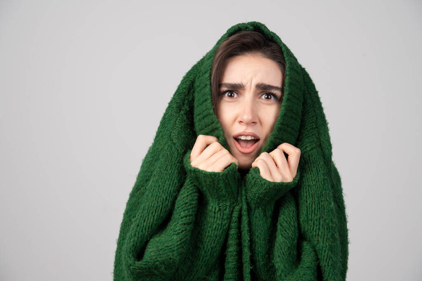 Egy fiatal nő zöld pulóverben megdöbbenve néz ki a szürke háttéren. Kiváló minőségű fénykép - Fotó, kép