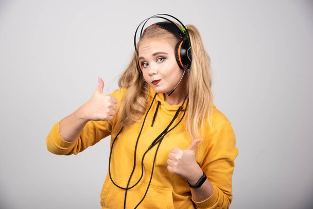 Woman in yellow sweatshirt giving thumbs up on gray background. High quality photo - Foto, afbeelding