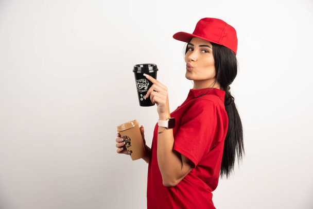 Female courier making kissy face with coffee cups. High quality photo - Φωτογραφία, εικόνα