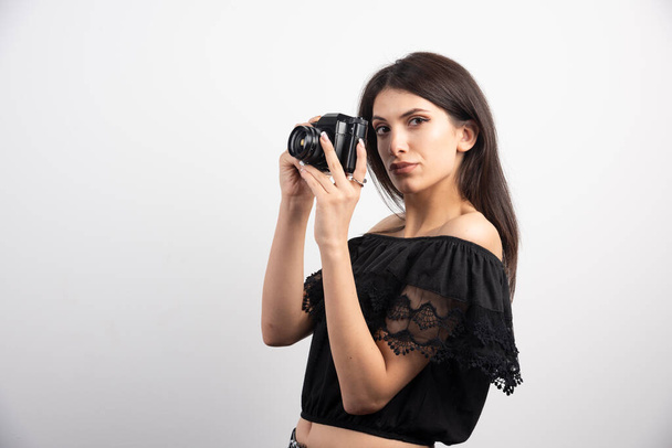 Όμορφη γυναίκα τραβάει φωτογραφίες με μια κάμερα σε λευκό φόντο. Υψηλής ποιότητας φωτογραφία - Φωτογραφία, εικόνα