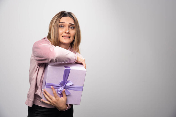 Blonde lady in pink sweatshirt holds a gift box and looks terrified. High quality photo - Photo, Image