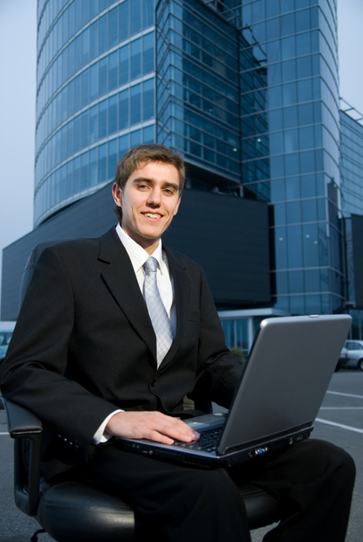 Uomo d'affari seduto di fronte all'edificio degli uffici e al lavoro sul suo computer portatile
 - Foto, immagini