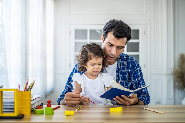 Portrait of young father teaching his cute little daughters' study. Excited smiling small child girl enjoying learning with pleasant dad at home. Children education, home schooling concept - Photo, Image