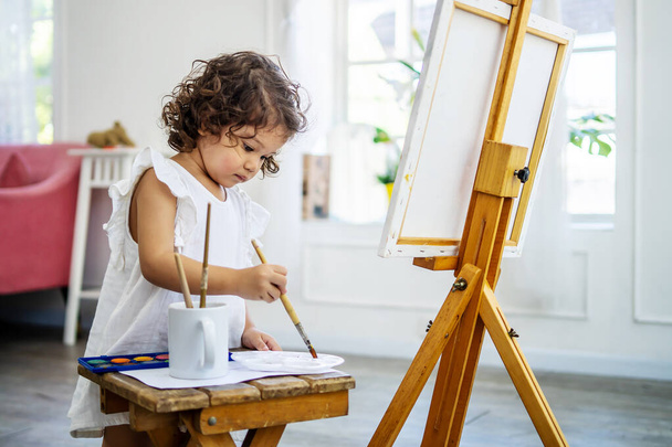 A little cute girl artist uses an acrylic paint brush to make her drawings on canvas - Foto, imagen