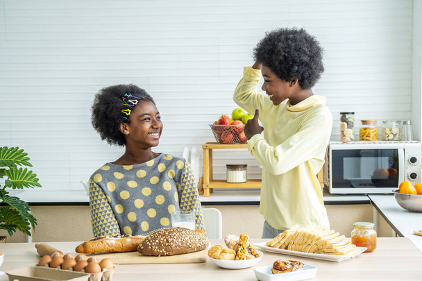 Zwei süße entzückende Geschwister afrikanisch-amerikanische Kinder beim Frühstück mit Milch in der Küche, Portrait des glücklichen Bruders, der Milch trinkt, zeigt Bizeps, um mit seiner Schwester zu erzählen, Essen und Trinken Gesundheitsfürsorge - Foto, Bild