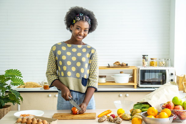 Manger sainement, afro-américaine heureuse fille faire le dîner et couper des tomates sur planche à découper avec couteau dans la cuisine - Photo, image