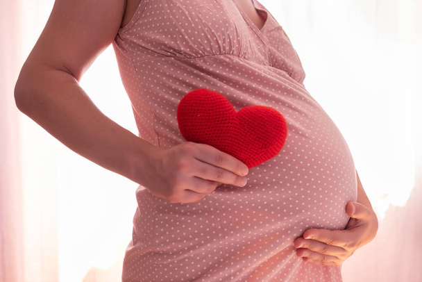 Těhotná žena s červeným symbolem srdce drží její břicho - Fotografie, Obrázek