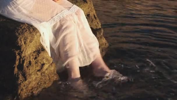 Женщина в белом платье, размахивающая водой с ногами на рассвете. Расслабляющее и трогательное море с водой из скалы на закате.  - Кадры, видео