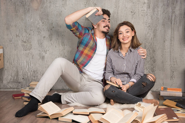 Bild eines hübschen Paares, das mit vielen Büchern auf dem Boden sitzt. Hochwertiges Foto - Foto, Bild