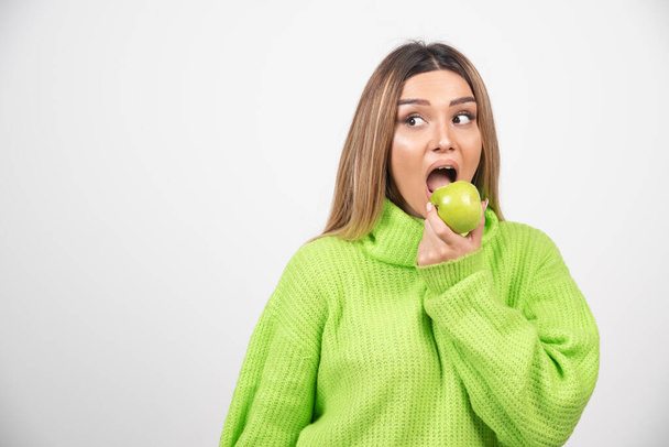 Młoda kobieta w zielonej koszulce jedząca jabłko. Wysokiej jakości zdjęcie - Zdjęcie, obraz