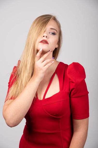 Femme blonde en tenue rouge touchant son menton. Photo de haute qualité - Photo, image