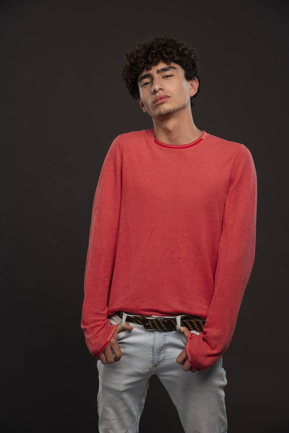 Nuori malli punaisessa paidassa poseeraa laittamalla kädet hänen taskuihinsa. Laadukas kuva - Valokuva, kuva